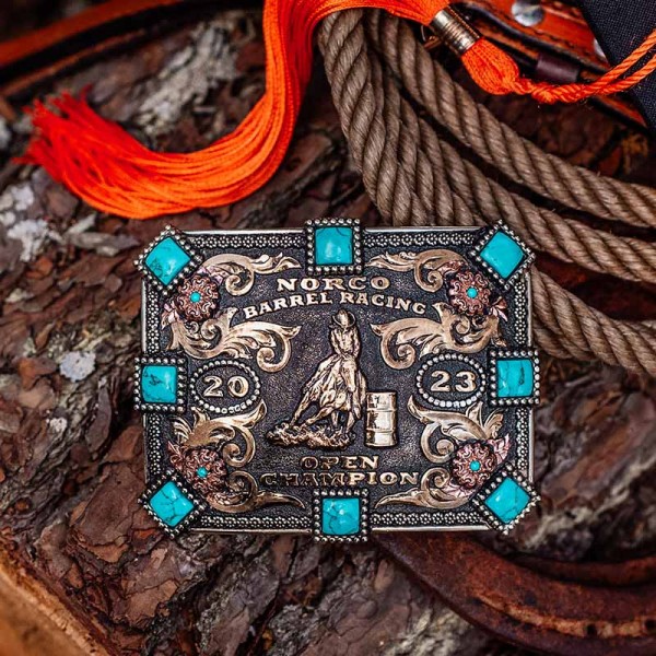 A custom women's rodeo belt buckle for Norco Barrel Racing Open Champion featuring turquoise stones and a barrel racer cowgirl figure